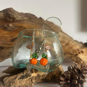 Peut inclure: Boucles d'oreilles pendantes avec des breloques citrouille orange, des accents verts et des cha&icirc;nes argent&eacute;es. Les boucles d'oreilles comprennent &eacute;galement des breloques en forme de feuille et des perles transparentes en forme de goutte.