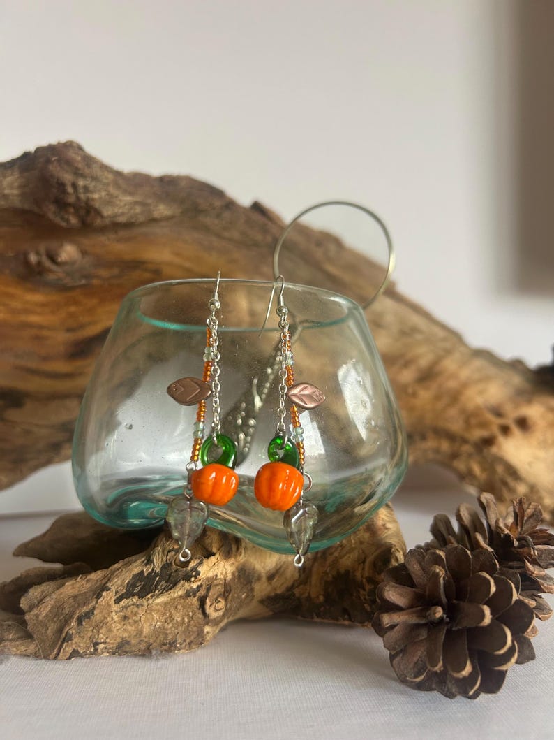 Peut inclure: Boucles d'oreilles pendantes avec des breloques citrouille orange, des accents verts et des cha&icirc;nes argent&eacute;es. Les boucles d'oreilles comprennent &eacute;galement des breloques en forme de feuille et des perles transparentes en forme de goutte.