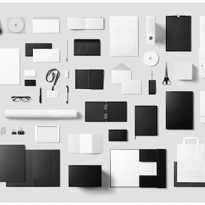 May include: A collection of black and white office supplies, including a clipboard, pens, CD, envelopes, notebooks, scissors, and a briefcase, arranged on a light gray surface. The items are neatly organized, creating a minimalist aesthetic.