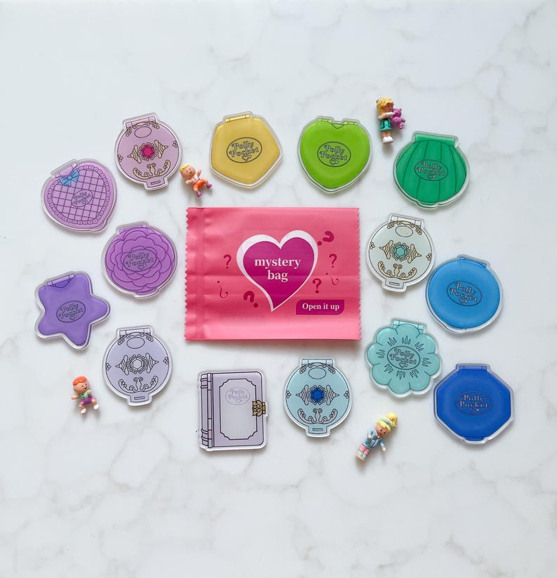 May include: A selection of vintage Polly Pocket compacts in diverse shapes and colours, such as hearts, stars, and shells, alongside miniature figures and a pink mystery bag with the text "mystery bag" and "Open it up".