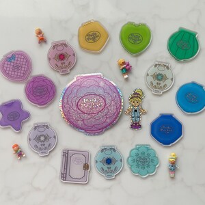 May include: A selection of vintage Polly Pocket toys in diverse shapes and colours, including compacts shaped like flowers, hearts, and shells. Several miniature figures are scattered among the compacts. The Polly Pocket logo is visible on many of the toys.