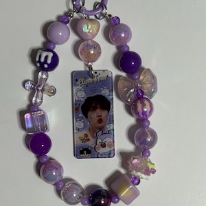 May include: A purple beaded keychain with a rectangular charm featuring a photo of a person. The keychain includes various purple beads, a cross, a heart-shaped bead, and a bow-shaped bead. The charm has the text "Class Four".