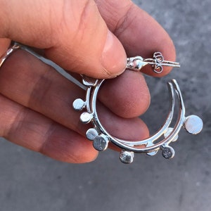 Può includere: Orecchini a cerchio in argento con un design circolare. Gli orecchini hanno una serie di piccoli cerchi attorno al cerchio.