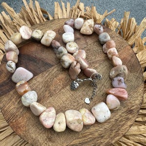 May include: A pink and white stone necklace with a silver clasp and a heart charm that says "Made with Love".