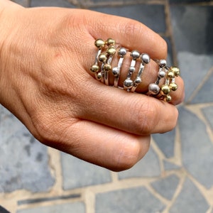 May include: A hand wearing a stack of silver and gold rings with small beads. The rings are stacked on top of each other and are all different sizes.
