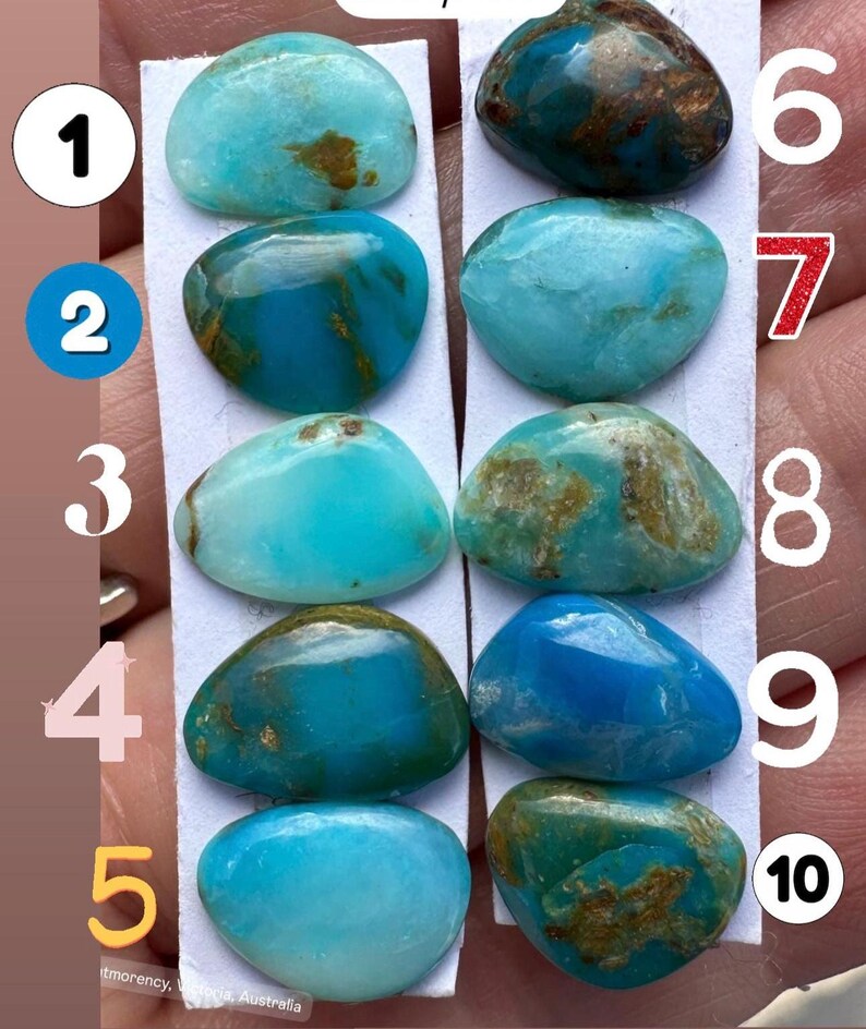 May include: Ten polished turquoise gemstones, each with unique patterns of blue and brown. The stones are oval-shaped and vary in shades of blue, from light to deep teal. The gemstones are displayed on white strips.