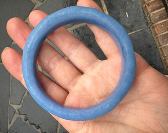 May include: A light blue bangle bracelet made of smooth, polished jade. The bracelet is round and has a simple design.