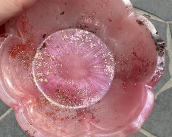 Könnte beinhalten: Eine rosa Blumenschale aus Harz mit glitzernder Oberfläche. Die Schale hat einen gewellten Rand und eine leicht erhöhte Mitte.