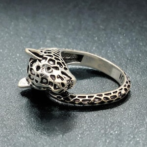 Könnte beinhalten: Silberfarbener Ring mit detailliertem Leopardenkopf-Design. Das Ringband hat ein strukturiertes Muster, und die Größe ist mit 10 markiert. Der Leopardenkopf hat ein geflecktes Muster.