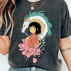 以下が含まれることがあります： アニメスタイルのカラフルなグラフィックが特徴のダークグレーのTシャツ。デザインには、若い女の子、ターコイズアクセントの白いドラゴン、ピンクの蓮の花が含まれています。このシャツは、快適でカジュアルなスタイルです。