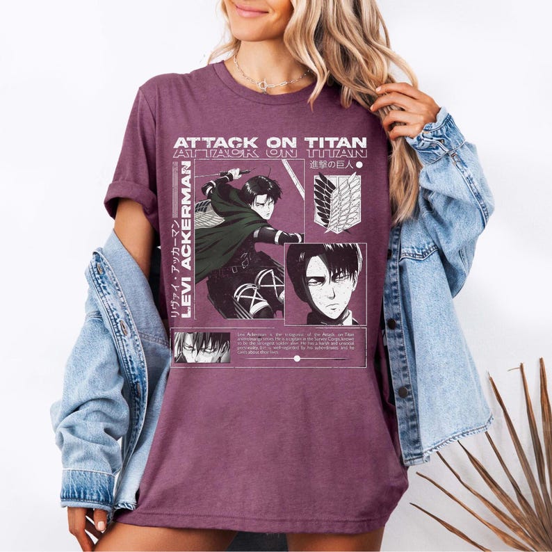 Pu&ograve; includere: T-shirt bordeaux con grafica della serie anime "Attack on Titan". Il design include il testo "Attack on Titan" e "Levi Ackerman" insieme a illustrazioni di personaggi in bianco e nero.