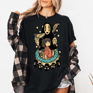 Może przedstawiać: Czarny t-shirt z kolorową grafiką z filmu animowanego Spirited Away. Projekt zawiera postacie takie jak No-Face, Chihiro i smoka, otoczone gwiazdami i innymi elementami. Wygodna, codzienna odzież.