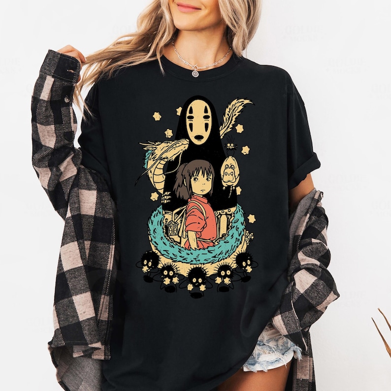 Może przedstawiać: Czarny t-shirt z kolorową grafiką z filmu animowanego Spirited Away. Projekt zawiera postacie takie jak No-Face, Chihiro i smoka, otoczone gwiazdami i innymi elementami. Wygodna, codzienna odzież.