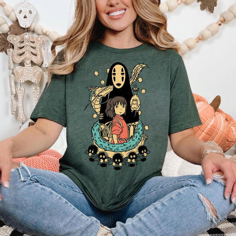 Może przedstawiać: Ciemnozielona koszulka z kolorową grafiką z filmu animowanego Spirited Away. Projekt zawiera postacie takie jak Bez Twarzy, Chihiro i duszki sadzy. Koszulka ma okrągły dekolt i kr&oacute;tkie rękawy.