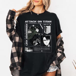 Pu&ograve; includere: T-shirt nero con grafica con la scritta bianca "ATTACK ON TITAN" e "LEVI ACKERMAN". Il design include illustrazioni in stile anime e testo giapponese. La maglietta &egrave; a girocollo e ha maniche corte.