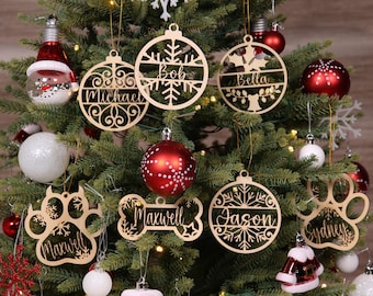 May include: A decorated Christmas tree with various ornaments. Includes wooden ornaments with names like "Michael", "Bob", "Bella", "Maxwell", "Jason", and "Sydney". Other ornaments are red, white, and silver. The tree is lit with small white lights.