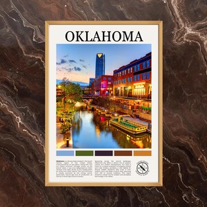 May include: A framed art print featuring a scenic view of Oklahoma City at dusk. The image showcases a river with a boat, buildings with illuminated windows, and the word "OKLAHOMA" at the top. The print has a gold frame and a color palette at the bottom.