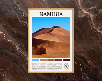 May include: Framed print featuring a photograph of the Namibian desert with a blue sky. The word "NAMIBIA" is at the top. A color palette is at the bottom. The print is in a gold frame and is displayed against a brown marble background.