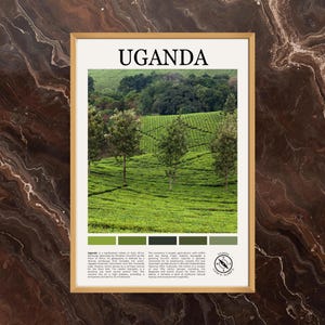May include: A framed print featuring the word "UGANDA" at the top. The image shows a green landscape with trees and a tea plantation. A color palette of greens is at the bottom. The print is in a gold frame.