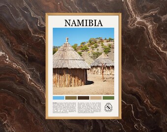 May include: Framed print featuring a landscape scene of Namibia. The image displays two traditional huts with thatched roofs and wooden walls under a clear blue sky. The word "NAMIBIA" is printed at the top. A color palette is included at the bottom.