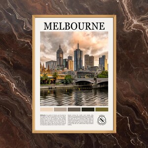 May include: A framed print featuring the Melbourne skyline under a cloudy sky. The word "MELBOURNE" is printed in bold, black letters at the top. The image includes a river, bridge, and buildings. A color palette is at the bottom.