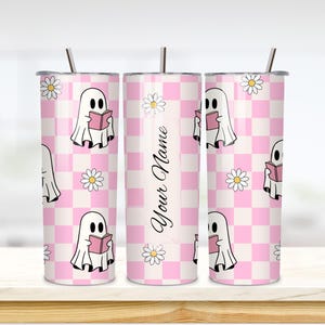 Puede incluir: Un juego de tres vasos de acero inoxidable con tapas y pajitas. Los vasos presentan un estampado de cuadros rosas y blancos con fantasmas de dibujos animados leyendo libros y flores de margarita. Un vaso tiene el texto "Your Name".