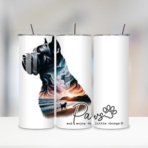 May include: White tumbler with a black dog silhouette and a landscape design. The design includes a beach scene with a small dog and the words "Paws and enjoy the little things" in a script font. A paw print is also included.