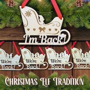 May include: Wooden Christmas sleigh ornaments with red ribbon hangers. The top ornament reads "I'm Back!" and the four below read "We're Back!". The phrase "Christmas Elf Tradition" is at the bottom.