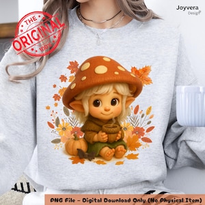 May include: A light gray sweatshirt featuring a whimsical illustration of a mushroom-capped character holding a cup, surrounded by autumn leaves and flowers. The design includes a small pumpkin and the text "PNG File - Digital Download Only (No Physical Item)".