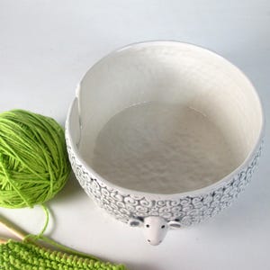 May include: White ceramic yarn bowl shaped like a sheep with black detailing. The bowl has a large opening and a smooth, white interior.