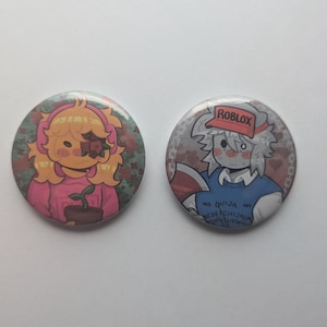 May include: Two round buttons with cartoon illustrations. One features a character with yellow hair, a pink outfit, and a plant. The other button has a character wearing a Roblox hat and a blue shirt, holding a book with text.