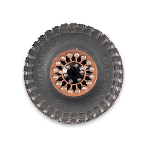 Puede incluir: Un neumático todoterreno negro y gris con un centro de color cobre. El neumático tiene un dibujo de la banda de rodadura texturizado y las palabras "Crawler Master" y "All Terrain" son visibles.