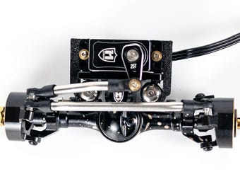 Puede incluir: Un conjunto de eje delantero para vehículo radiocontrolado en metal negro, con un servomotor montado con brazo de 25T, varillajes de dirección plateados y una carcasa de diferencial moteada, incluyendo soporte negro y tornillos visibles.