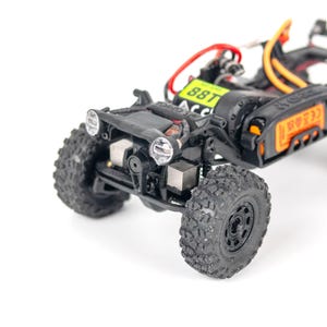以下が含まれることがあります： 黒とグレーのミニチュアのラジコンカーのクローズアップ。 大きなテクスチャードタイヤ、ヘッドライト、および目に見える内部コンポーネントを備えています。 バッテリーには「88T」と表示されています。