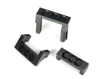 Pode incluir: Três suportes de plástico preto, cada um com três aberturas circulares. Os suportes têm uma base retangular e um design em forma de U com uma série de pequenos orifícios nas laterais. Os objetos estão em um fundo branco.