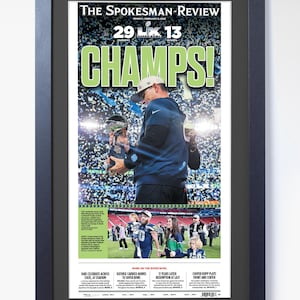 Peut inclure: Une page de couverture encadrée du journal The Spokesman-Review, célébrant une victoire au Super Bowl. Le titre est "CHAMPS!" en grandes lettres vertes, avec le score 29-13. L'image montre un entraîneur tenant un trophée.