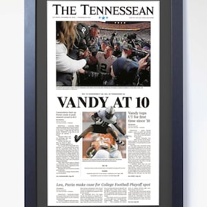 May include: A framed newspaper front page from The Tennessean, with the headline "VANDY AT 10." The image shows a football game photograph and text detailing the game's results. The frame is black, and the paper is dated.