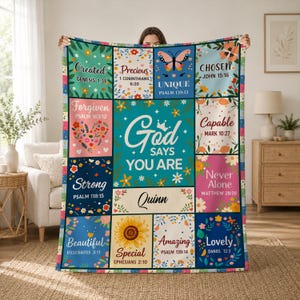 May include: A rectangular throw blanket featuring a grid of colorful panels with floral patterns and religious text. The center panel reads God Says You Are with the name Quinn below. Each surrounding block contains a word like Chosen, Strong, or Lovely paired with a Bible verse reference and decorative illustrations.