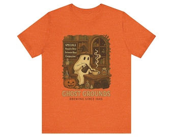 Può includere: T-shirt arancione con un'illustrazione di un fantasma che prepara il caffè in un ambiente accogliente. Il design include una zucca, un gatto nero e il testo "Ghost Grounds Brewing Since 1666". La maglietta elenca anche "Pumpkin Brew", "Enchanted Blend" e "Catpuccino".