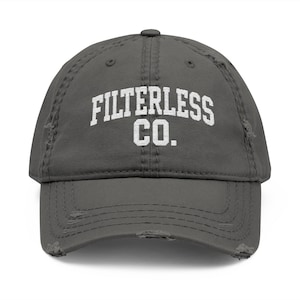 May include: A distressed charcoal grey baseball cap featuring the white text "FILTERLESS CO." in a block font. The cap has a curved peak and a worn, distressed look.