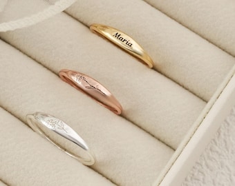 Op de afbeelding: Drie gepersonaliseerde ringen in goud, roségoud en zilver, elk met een uniek ontwerp. De gouden ring is gegraveerd met de naam "Maria". De ringen worden gepresenteerd in een witte sieradendoos.