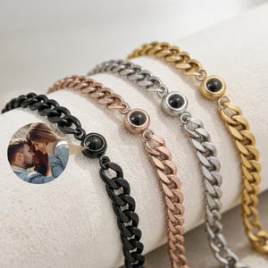 Può includere: Una collezione di braccialetti a catena a maglia in nero, oro rosa, argento e oro. Ogni braccialetto presenta una pietra nera rotonda e un design a maglie. Una piccola foto è inserita a sinistra.