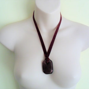 May include: A burgundy velvet ribbon necklace with a dark brown pendant. The pendant is a rectangular shape with rounded edges.