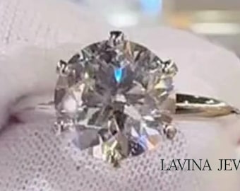 May include: A sparkling diamond ring with a large, round-cut center stone. The ring is set on a delicate silver band and held by a gloved hand. The text "LAVINA JEWEL" is visible.