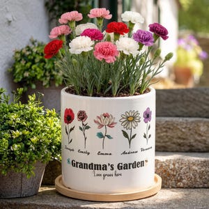 May include: A white ceramic planter with a wooden base, filled with colorful carnations. The planter is decorated with floral illustrations and the text "Grandma's Garden" and "Love grows here".