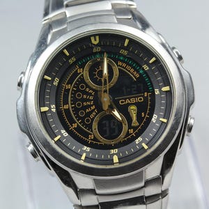 May include: A silver-toned Casio digital watch with a black face and gold accents. The watch features a digital display, multiple dials, and the Casio logo. The watch band is also silver-toned.