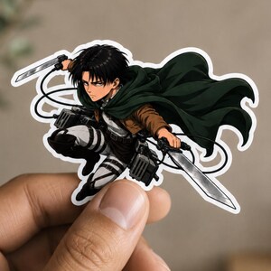 May include: A die-cut vinyl sticker featuring an anime character with black hair, wearing a dark green cape, brown jacket, and white pants with straps. The character is in a dynamic pose, holding two silver blades and equipped with gear.