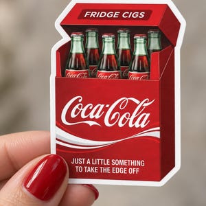 Könnte beinhalten: Ein gestanzter Aufkleber, der eine rote Zigarettenschachtel mit sechs Coca-Cola-Glasflaschen zeigt. Die Packung trägt oben den Text FRIDGE CIGS, in der Mitte das Coca-Cola-Logo und den Satz JUST A LITTLE SOMETHING TO TAKE THE EDGE OFF.