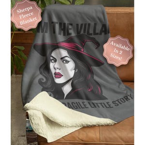 May include: Gray sherpa fleece blanket featuring a witch illustration with a black hat and red accents. The text "I'M THE VILLAIN" and "FRAGILE LITTLE STORY" are printed on the blanket. Available in two sizes.