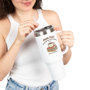 May include: White travel mug with a handle and a silver lid. The mug features the text "Mom Fuel: Powered by Coffee & Quiet" along with a graphic of a coffee cup on top of books. A clear straw is inserted into the lid.